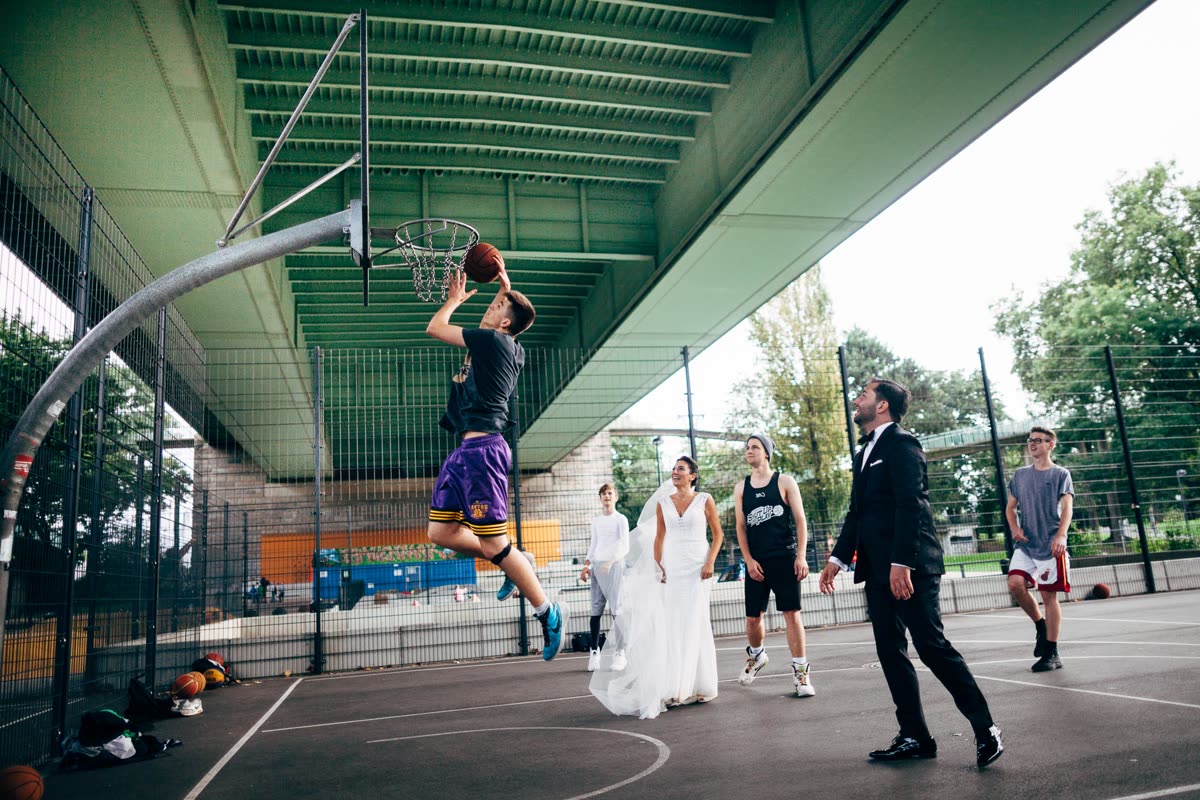 Basketballplatz unter einer Brücke: Ein Spieler springt zum Korb, Braut und Bräutigam stehen mitten auf dem Feld.