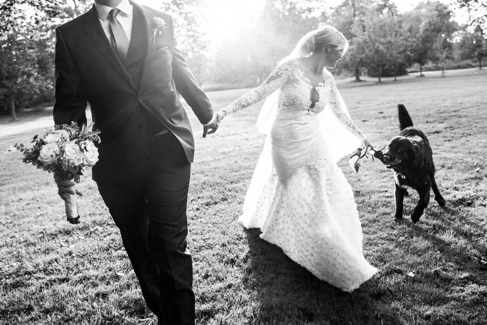 Schwarzweißfoto: Brautpaar auf einer Wiese, der Hund beißt der Braut in den Schuh.